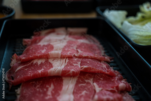 Close up shot of rare sliced beef with marbled texture on a black plate. Asian shabu shabu sukiyaki food style.