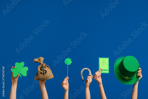 Female hands holding greeting card and party decor for St. Patrick's Day celebration on blue background celebration