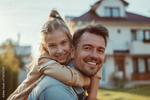 Daughter on father's shoulder, mother smiling, happy, family fun time with father and in front of the house in the morning.