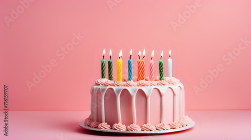 Birthday cake with colorful candles on pink background.