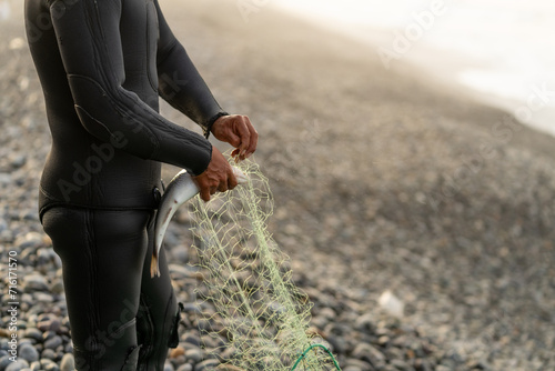 Fisherman in wetsuit unhooking a caught fish from the net