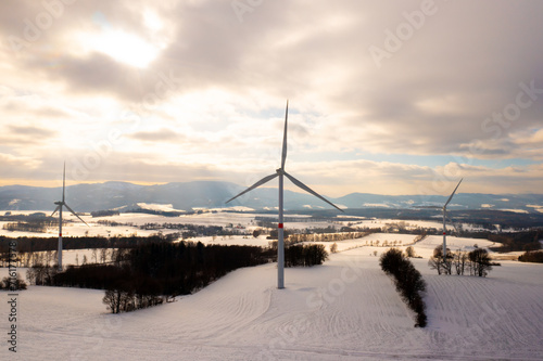 Panoramic view of wind turbines or wind mills on winter field against cloudy sky during sunset