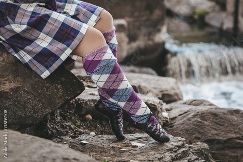 Woman in purple and blue tartan skirt and long woolen socks sitting on rocks beside waterfall in autume photo