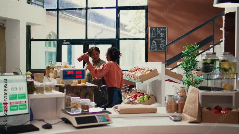 Merchant offering food sample to regular customer, ensuring organic healthy ingredients for sustainable lifestyle. Client choosing bio products at zero waste eco store. Handheld shot. Merchant offering food sample to regular customer, ensuring organic healthy ingredients for sustainable lifestyle. Client choosing bio products at zero waste eco store. Handheld shot.