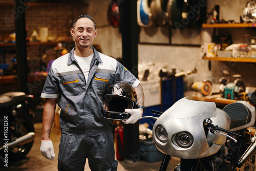 Portrait of smiling mechanic standing next motorcycle in his garage