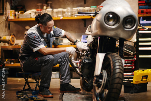Mechanic in uniform repairing motorcycle of client
