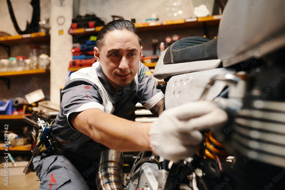 Experienced mechanic in uniform repairing motorbike in garage, small business concept
