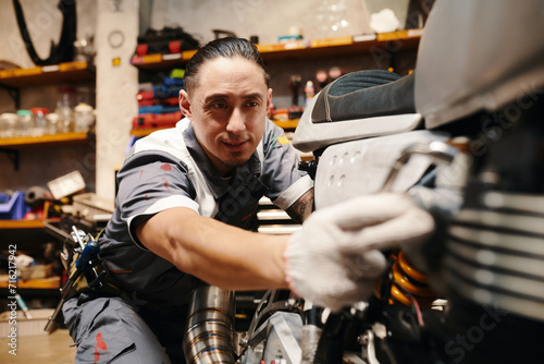 Experienced mechanic in uniform repairing motorbike in garage, small business concept