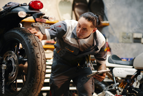 Repairman checking wheels and tires of motorcycle in garage © DragonImages