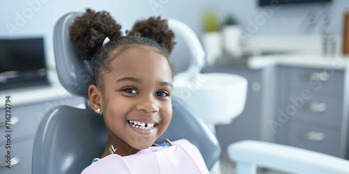 African American elementary school girl sitting in dentist chair exposing white teeth. Creative banner with happy child kid for pediatric dentistry. Children treatment teeth, medical checkup concept
