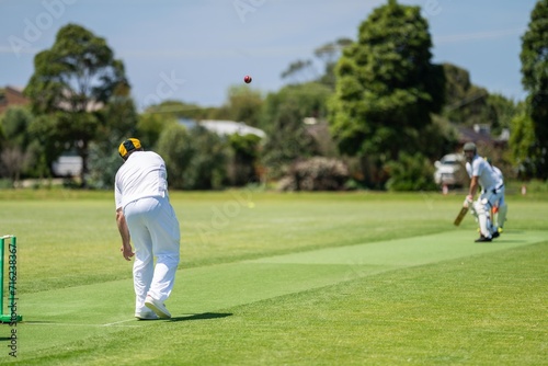 a local cricket match being played on a green cricket oval in summer in australia. australian cricketer batting and bowling in a game