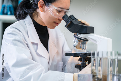 Close up of researcher, geologist or archaeologist working with microscope and laptop studying, finding or discovering soil, rock, stone or fossil sample in paleontology, archaeological and geological