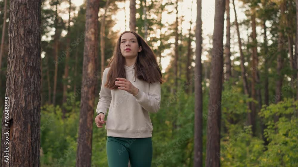 Solitary female jogger runs in forest at sunset. Woman with long loose hair maintains body shape in evening. Active jogging to improve physical endurance in nature Solitary female jogger runs in forest at sunset. Woman with long loose hair maintains body shape in evening. Active jogging to improve physical endurance in nature
