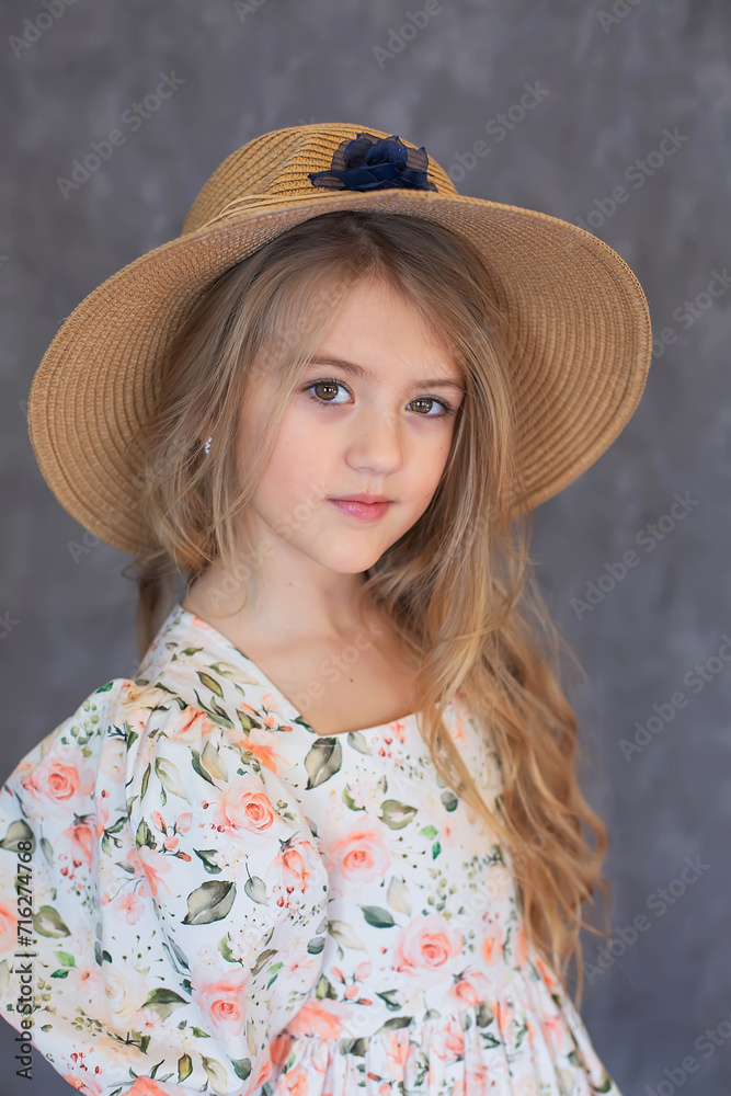 a beautiful long-haired blonde girl in a floral dress and a straw hat on a gray background