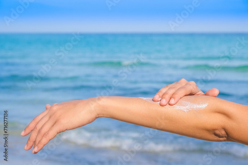Woman applying sunscreen and taking care of her skin to protect her skin from UV rays She applies sunscreen on her hands and arms. Very sunny sea background Health and skin concept