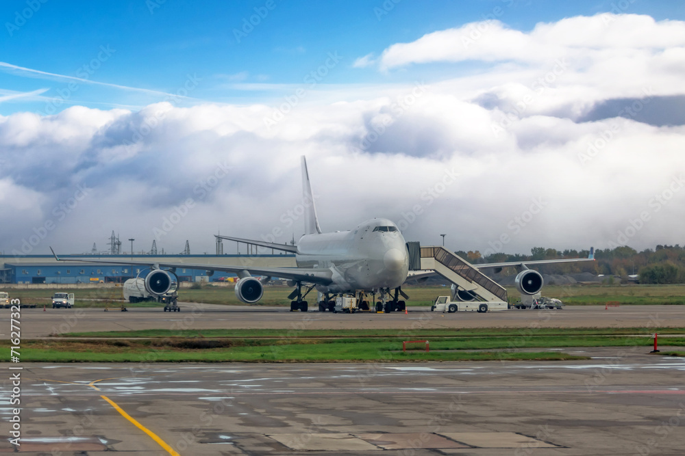 Large cargo plane parking preparation for flight loading food and goods. Large clouds of fog in the background Large cargo plane parking preparation for flight loading food and goods. Large clouds of fog in the background