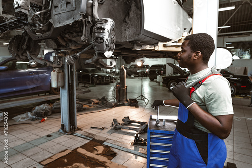 African male auto-mechanic repairing car brakes under the car in auto service photo