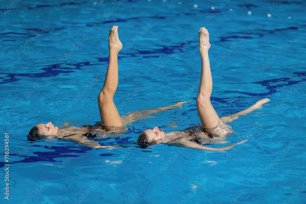 Aquatic poetry of a synchronized swimming duet, crafting a mesmerizing dance in the shimmering pool waters, a perfect blend of grace and precision