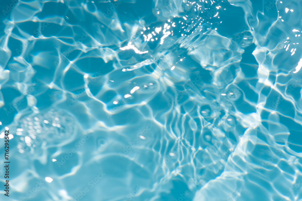 Bluewater waves on the surface ripples blurred. Defocus blurred transparent blue colored clear calm water surface texture with splash and bubbles. Water waves with shining pattern texture background.