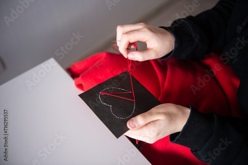 The child's hands make a card with a heart for mother's Day with red threads photo