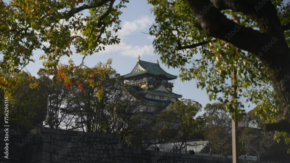 Japanese castle during golden hour surrounded by trees with leaves moving in the wind on a spring day in Osaka, Japan. Japanese castle during golden hour surrounded by trees with leaves moving in the wind on a spring day in Osaka, Japan.