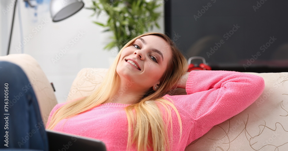 young beautiful blond woman lie on the sofa in livingroom hold tablet in arms sunny morning concept young beautiful blond woman lie on the sofa in livingroom hold tablet in arms sunny morning concept