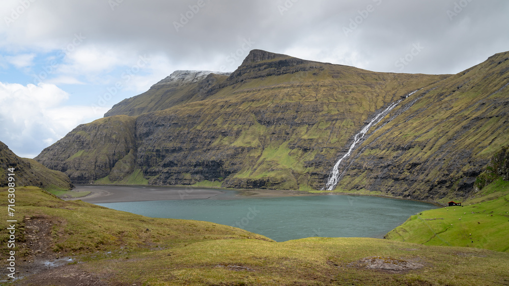 Saksun lake, surrounded by green hills and cliffs and a waterfall. Landscape and lake from Village of Saksun located on the island of Streymoy, Faroe Islands, Denmark