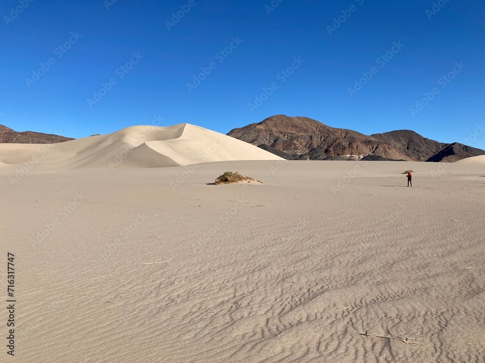 Lone hiker crossing sand dunes under blue sky