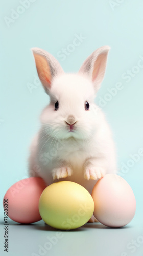 Adorable white bunny posing with colorful pastel Easter eggs on a blue background.