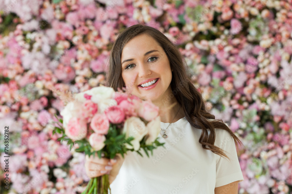 Beautiful female model with rose flower in her hand standing on blooming floral blossom background. Love, 8 march, birthday and holiday woman portrait