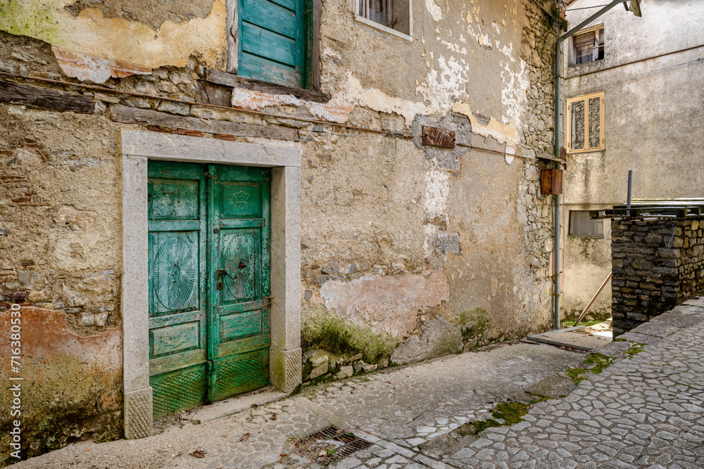 Vintage green front door facing on an alley of an almost abandoned Italian mountain village. Canalaz, Grimacco, Udine province, Friuli Venezia Giulia, Italy. Urbex photography.