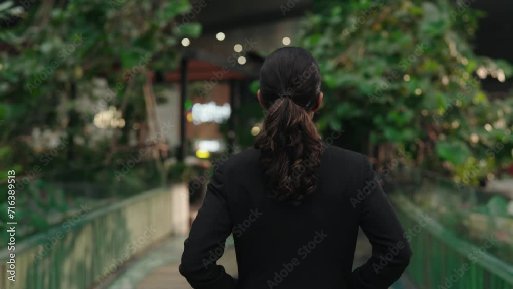 Back View of Successful Female Leader with Her Hands in Her Pockets and Walking Around the Business Center Alone. Back View of Successful Female Leader with Her Hands in Her Pockets and Walking Around the Business Center Alone.