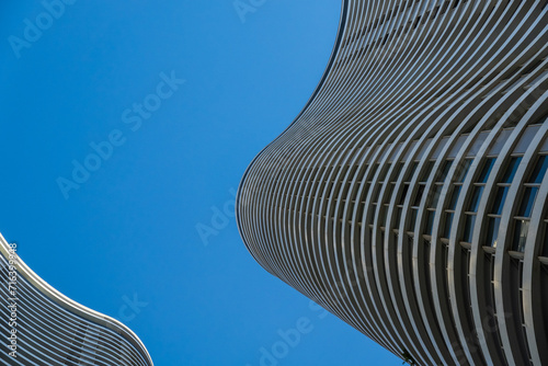 Curvilinear modern skyscrapers soar against a clear blue sky, showcasing contemporary architectural elegance and urban skyline.
