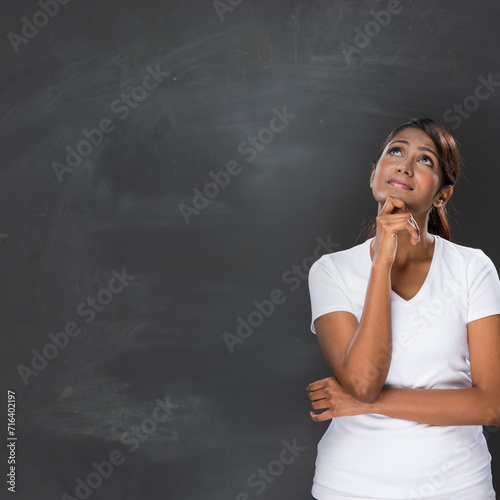 Happy Indian woman standing in front of a blank chalkboard.