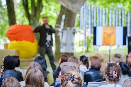 Informal outdoor event with a dynamic speaker engaging with a diverse audience seated in a park.