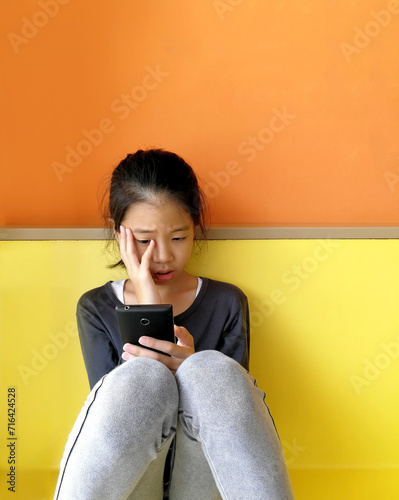 Asian child girl with serious face using smart phone too much screen time, absorbed with cell phone. Concept of children's screen addiction, hooked on mobile, smartphone addiction or excessive phone.