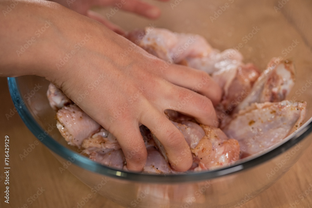 A hand mixes raw chicken wings with spices. Preparation of ingredients.