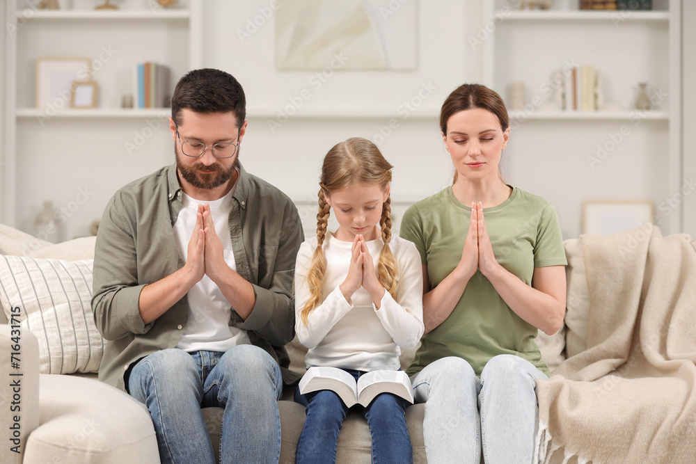 Girl and her godparents praying together on sofa at home Girl and her godparents praying together on sofa at home