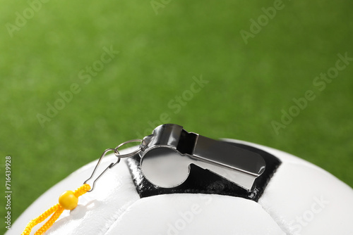 Football referee equipment. Soccer ball and metal whistle on green grass  closeup with space for text