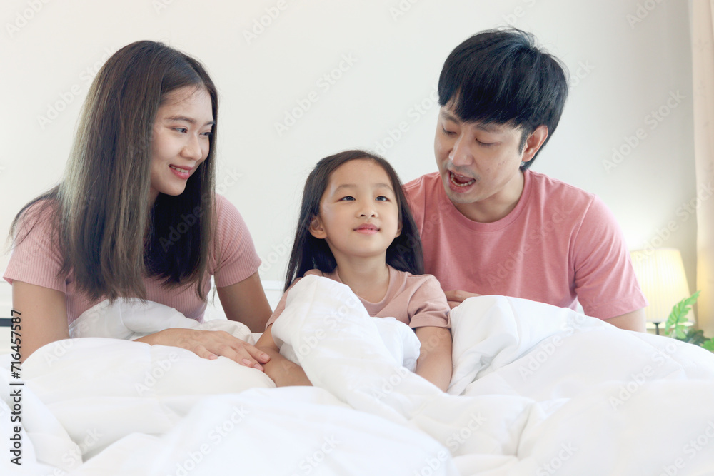 Happy Asian family has fun in bedroom. Father, mother daughter cover body with blanket during lying together on white bed. Parents and kid child girl have good memory at home. parenthood and childhood Happy Asian family has fun in bedroom. Father, mother daughter cover body with blanket during lying together on white bed. Parents and kid child girl have good memory at home. parenthood and childhood