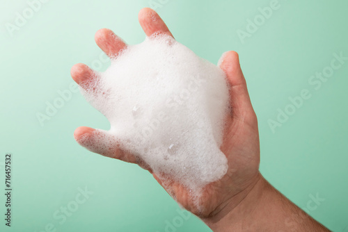 Thick foam in a man's hand on a turquoise background.