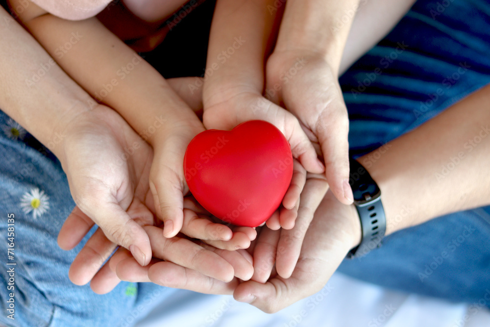 Top view of mother, father and daughter holding red heart in hands, family celebrating together, child girl, mom and dad holding red heart with love. Happy family relationships and health care concept