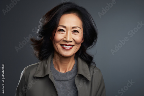 Asian smiling middle aged woman on grey background.