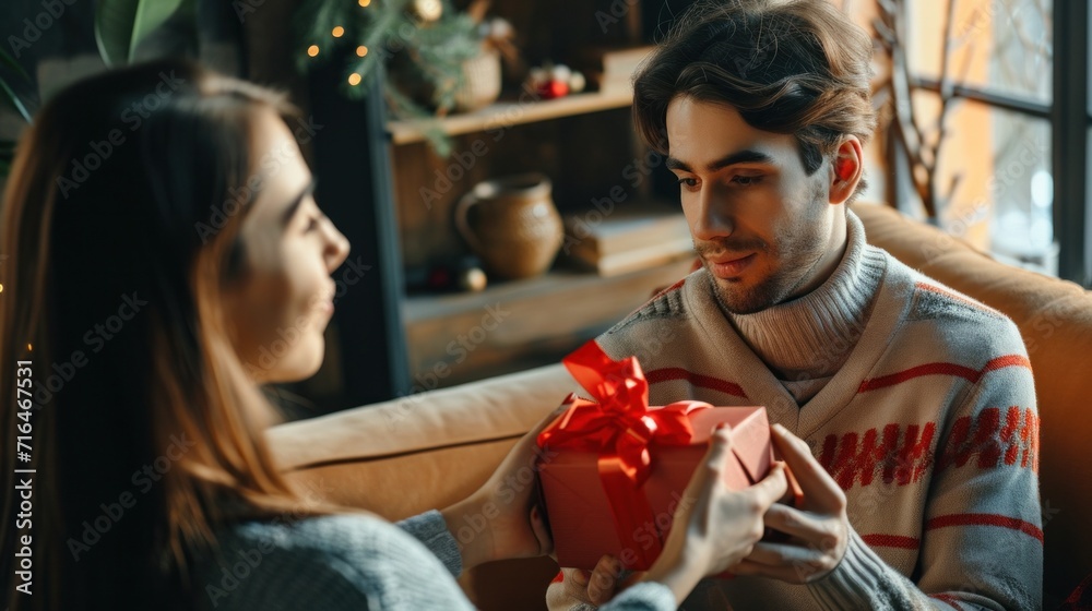 Young man is giving a present to his lovely girlfriend while they are sitting on couch at home Young man is giving a present to his lovely girlfriend while they are sitting on couch at home