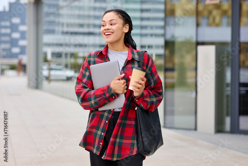 An African-American student smiles while posing on the street with a laptop. Rest while studying.