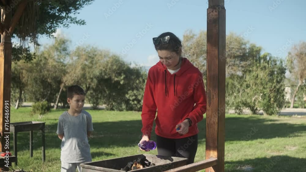 The family is in nature, they make a fire in the barbecue to make a barbecue, mom pours liquid on the coals for ignition The family is in nature, they make a fire in the barbecue to make a barbecue, mom pours liquid on the coals for ignition