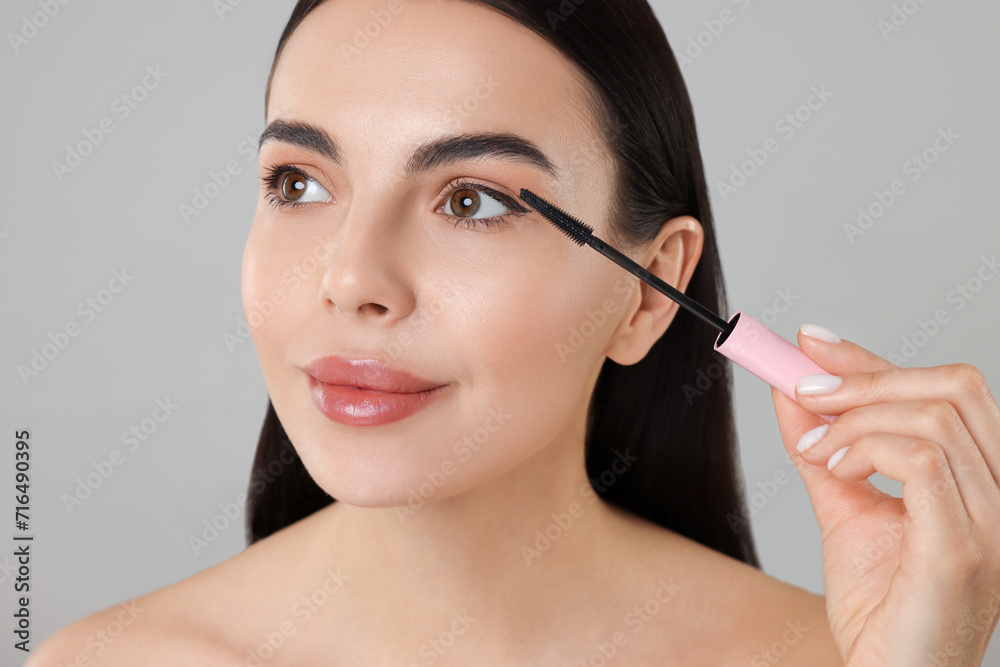 Beautiful young woman applying mascara on grey background, closeup Beautiful young woman applying mascara on grey background, closeup