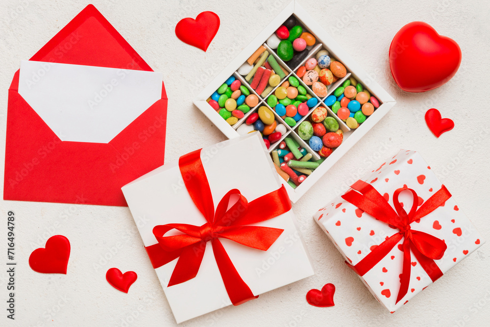Red envelope with candy and gift box and Valentines hearts on colored background. Flat lay, top view. Romantic love letter for Holiday concept Red envelope with candy and gift box and Valentines hearts on colored background. Flat lay, top view. Romantic love letter for Holiday concept