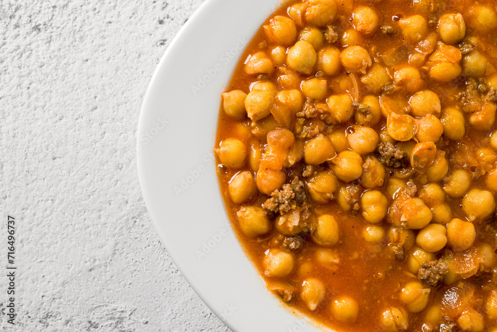 Chickpea stew with minced meat on a white porcelain plate on a stone table Chickpea stew with minced meat on a white porcelain plate on a stone table