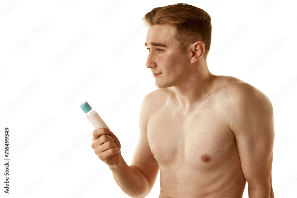 Fototapeta premium Shirtless handsome young guy holding face moisturizing cream jar isolated over white background. Morning spa. Concept of male beauty, skin care, cosmetology and cosmetics, health
